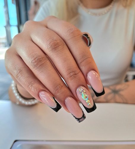 A close-up of a hand showcasing stylish long nails with a pink base and black tips.