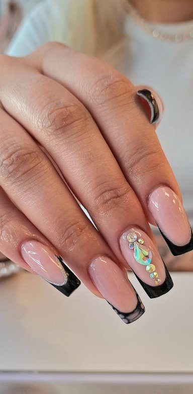 A close-up of a manicured hand with pink and black nails and a rhinestone accent.