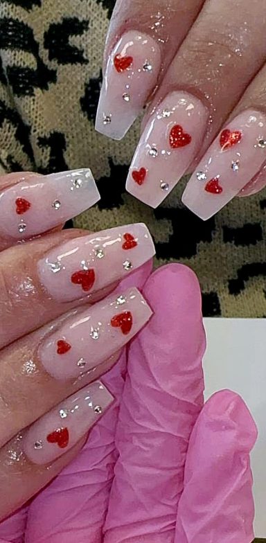 Nail design featuring a pink base with red hearts and silver embellishments.