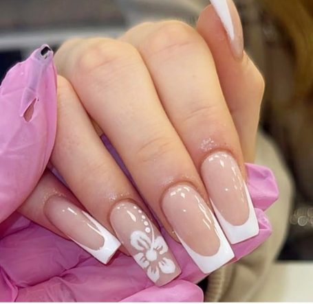 Manicured nude nails with white tips and a floral design on one nail.